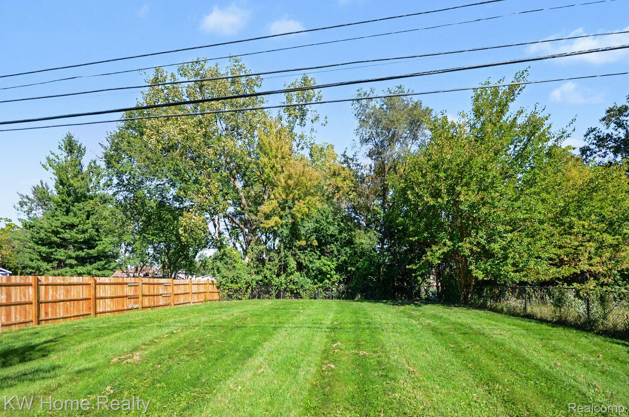 2383 East Maple Road Troy, MI 48083 - Photo 21 of 25 Expansive grassy yard with a wooden privacy fence, chain-link fence, and mature trees