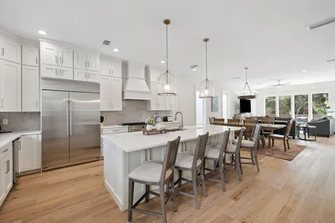 a kitchen with stainless steel appliances kitchen island granite countertop a dining table chairs stove refrigerator and cabinets