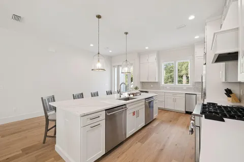 a kitchen with stove a sink dishwasher a refrigerator and white cabinets with wooden floor