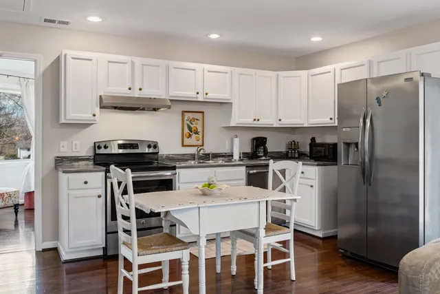 a kitchen with stainless steel appliances kitchen island granite countertop a refrigerator a stove a sink a dining table and chairs with wooden floor