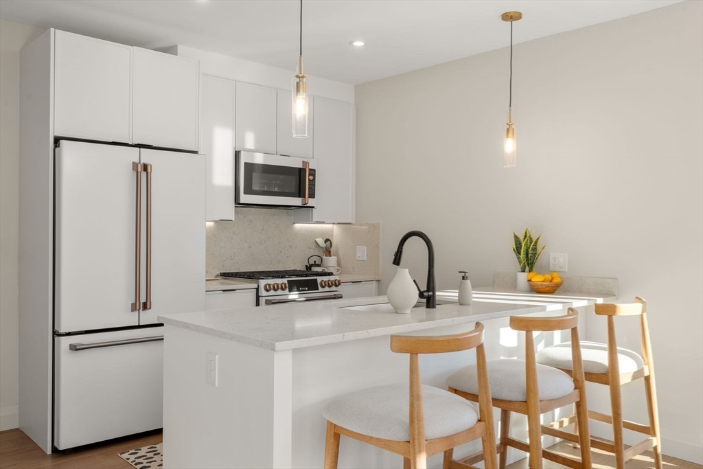 100 Lincoln Street, Unit 403 Boston, MA 02135 - Photo 12 of 23 a kitchen with stainless steel appliances a refrigerator a sink a stove a dining table and chairs