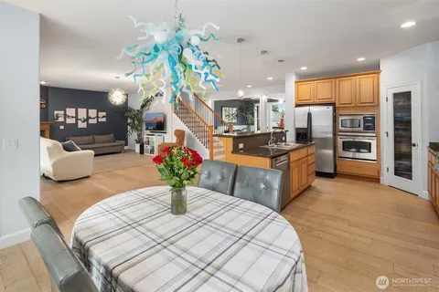 a kitchen with stainless steel appliances kitchen island granite countertop a stove a refrigerator a sink dishwasher and a dining table with wooden floor