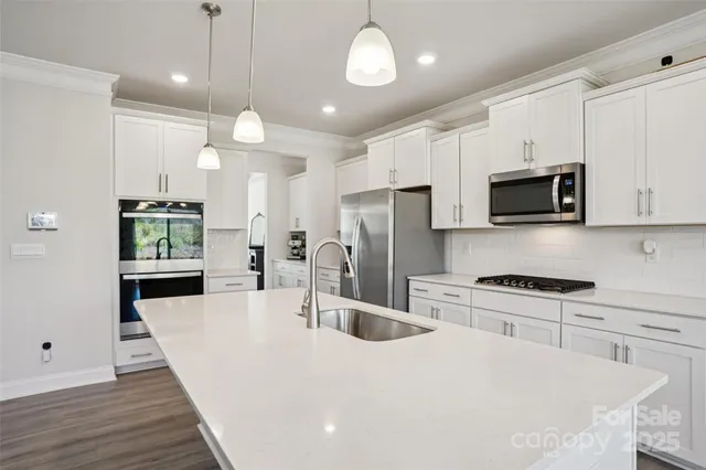 a kitchen with stainless steel appliances kitchen island granite countertop a stove a refrigerator a oven a sink a refrigerator white cabinets and wooden floor