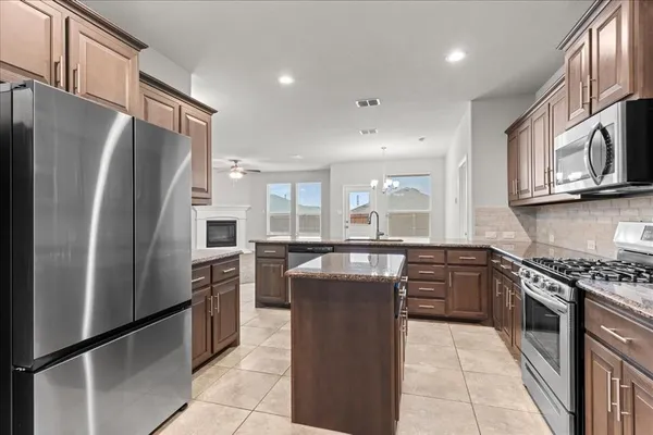 a kitchen with stainless steel appliances granite countertop a refrigerator a stove a sink a microwave and island