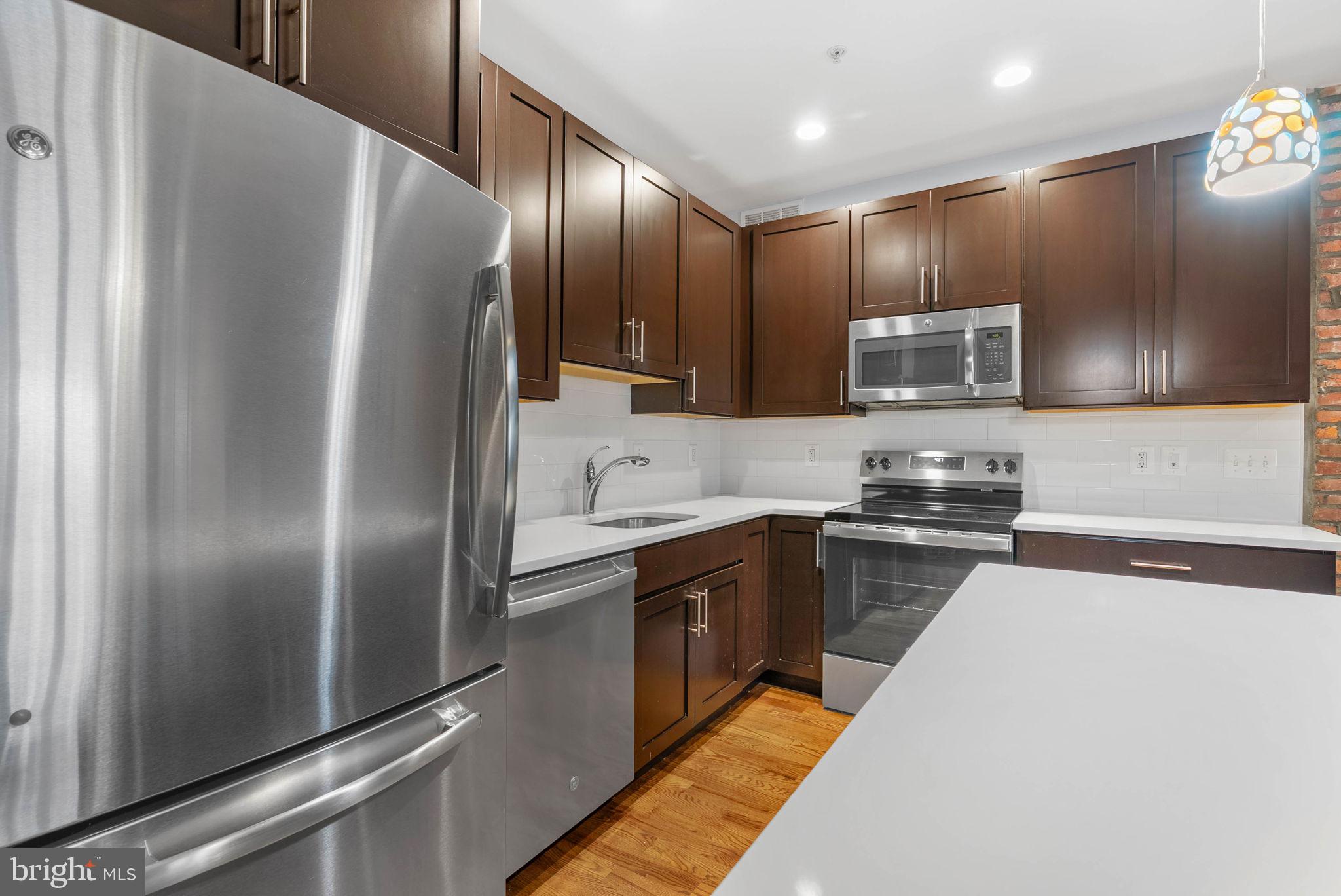 924 South 11th Street, Unit 101 Philadelphia, PA 19147 - Photo 11 of 27 a kitchen with stainless steel appliances granite countertop a refrigerator a stove and a sink with wooden floor