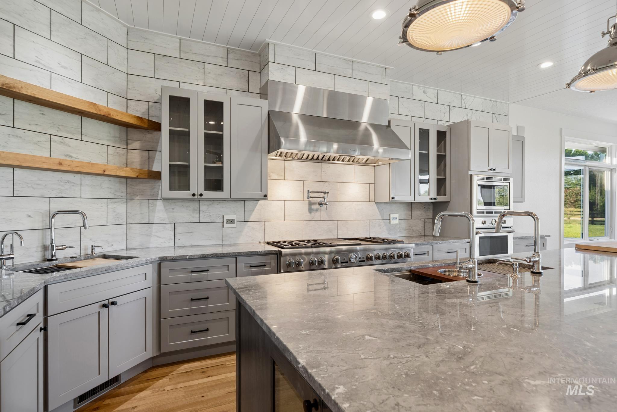 2050 Artesian Road Eagle, ID 83616 - Photo 10 of 49 Gourmet kitchen featuring a large central island with integrated appliances and pendant lighting, stainless steel range hood, full tile backsplash, and light wood-finish flooring
