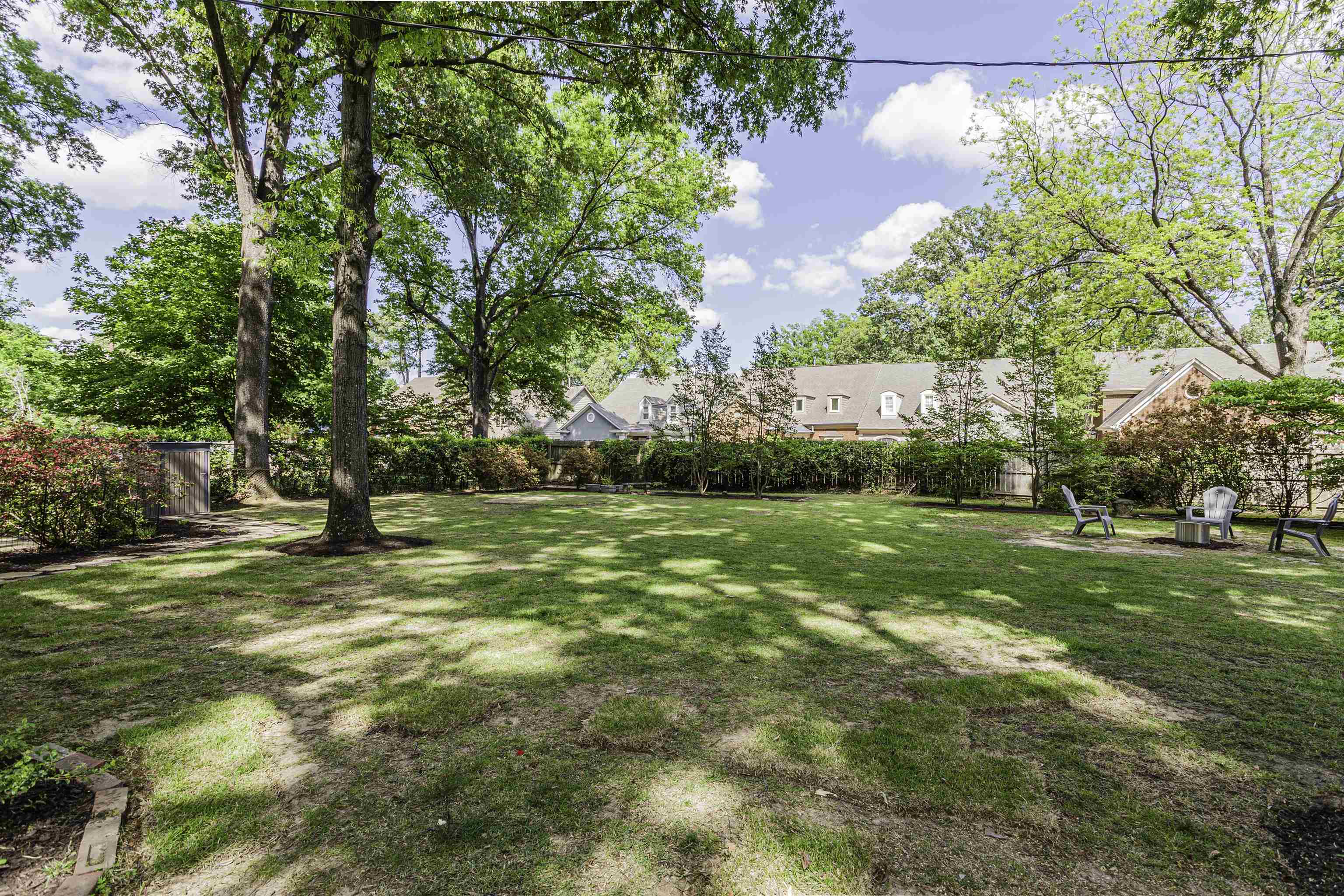 480 Colonial Road Memphis, TN 38117 - Photo 15 of 16 Expansive green lawn surrounded by mature trees and shrubs, featuring a wood-panel utility shed, a defined planting bed, and a natural privacy screen