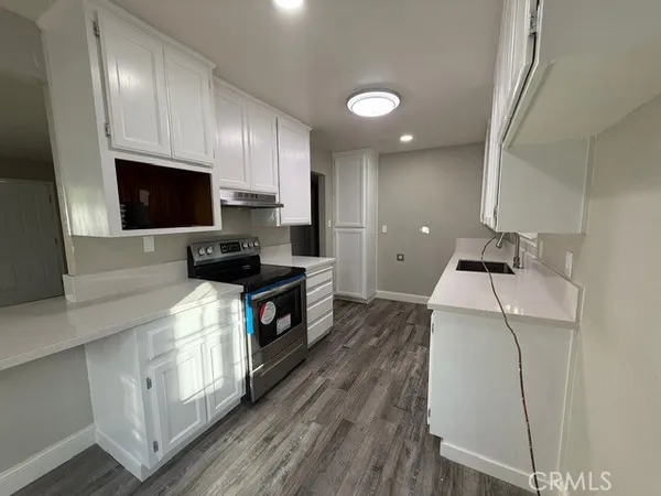 a kitchen with granite countertop a sink a stove top oven and cabinetry