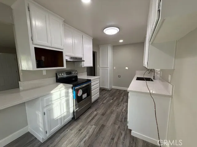 a kitchen with granite countertop a sink a stove top oven and cabinetry