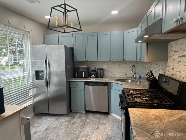 a kitchen with stainless steel appliances granite countertop a refrigerator a sink a stove and white cabinets