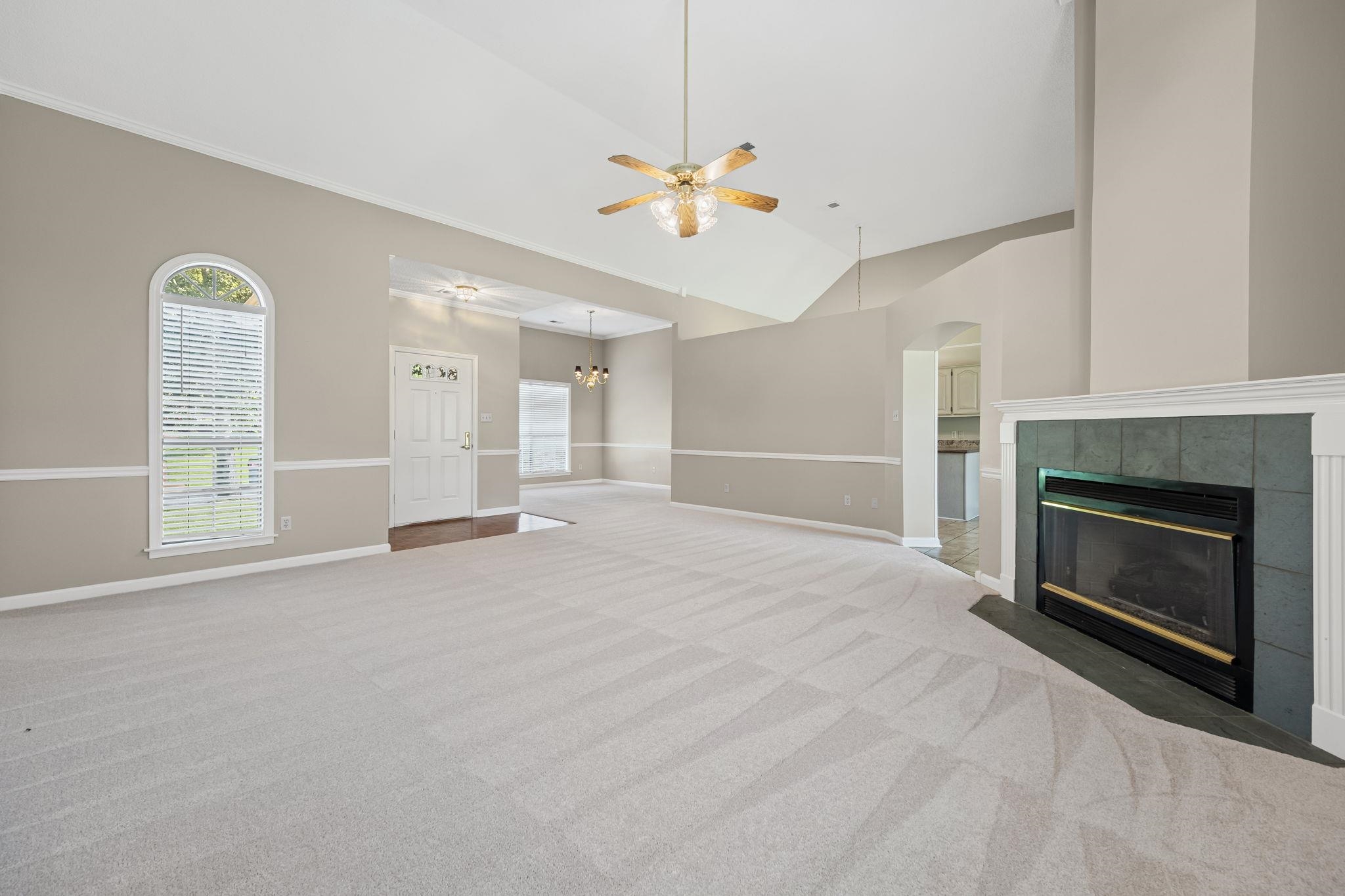 8409 Ridge Fall Cove Memphis, TN 38018 - Photo 4 of 28 Unfurnished living room featuring a ceiling fan, carpet, a fireplace, vaulted ceiling, and arched walkways