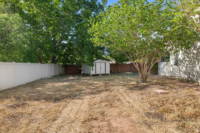 20 Valley Road Leeds, UT 84746 - Photo 38 of 57 Spacious backyard featuring a white vinyl privacy fence, mature trees providing natural shade, a storage shed, and a section of brown wood fencing