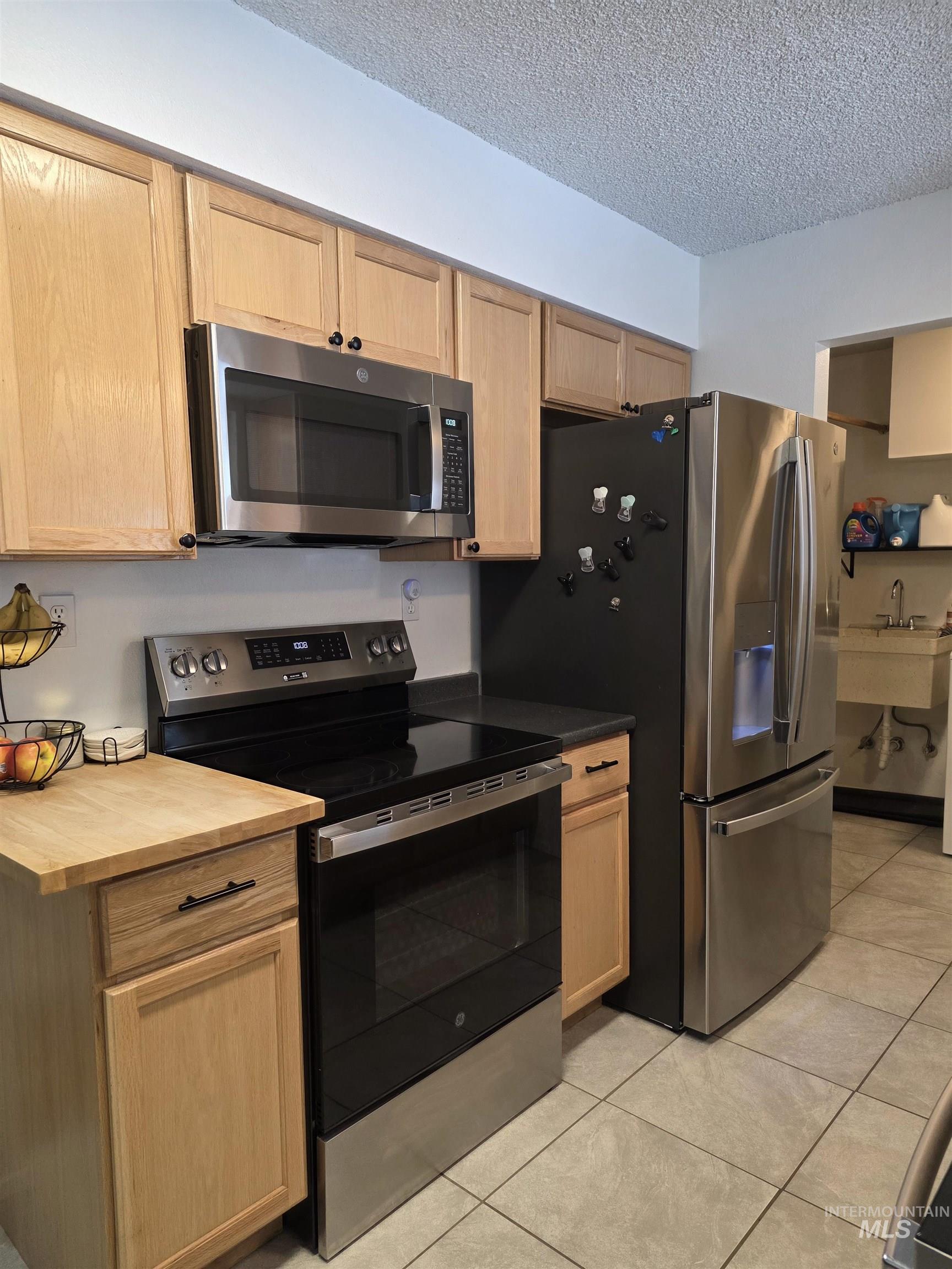 179 Timberline Drive Pierce, ID 83546 - Photo 14 of 24 Kitchen featuring appliances with stainless steel finishes, light brown cabinetry, light tile patterned flooring, a textured ceiling, and butcher block countertops