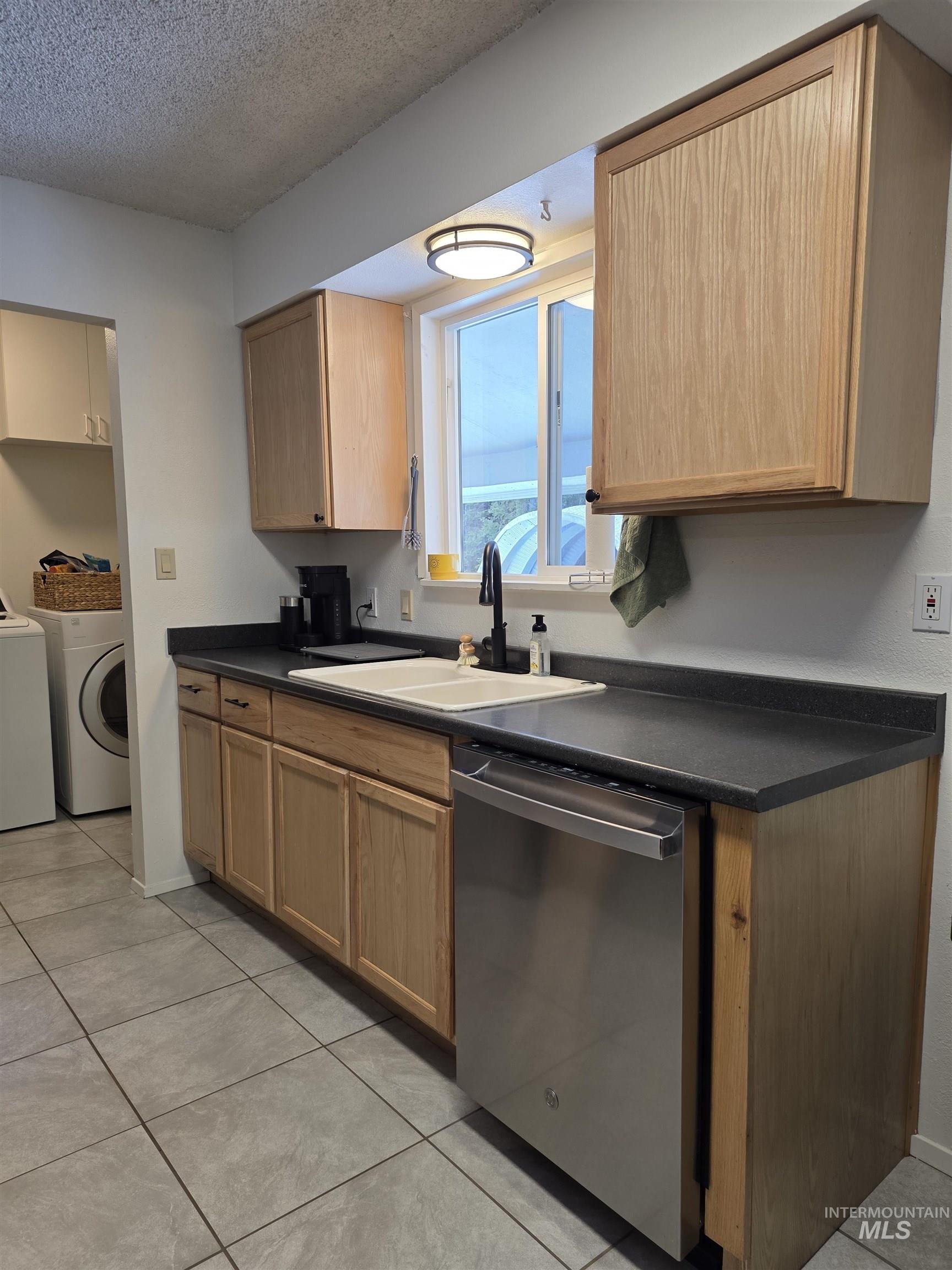 179 Timberline Drive Pierce, ID 83546 - Photo 16 of 24 Kitchen featuring dark countertops, dishwasher, a textured ceiling, washer / dryer, and light tile patterned flooring
