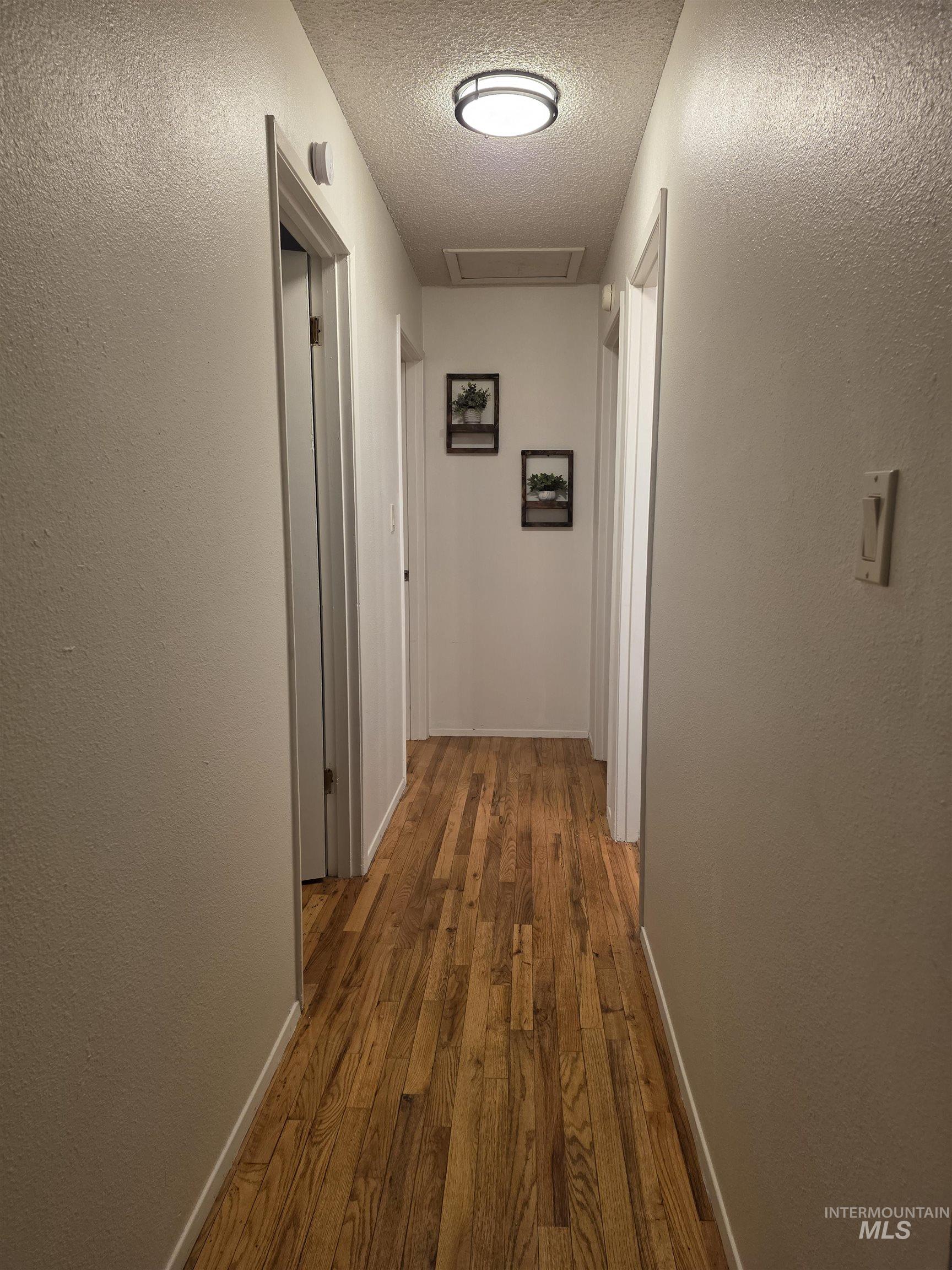 179 Timberline Drive Pierce, ID 83546 - Photo 19 of 24 Hallway featuring a textured wall, a textured ceiling, wood-type flooring, and attic access