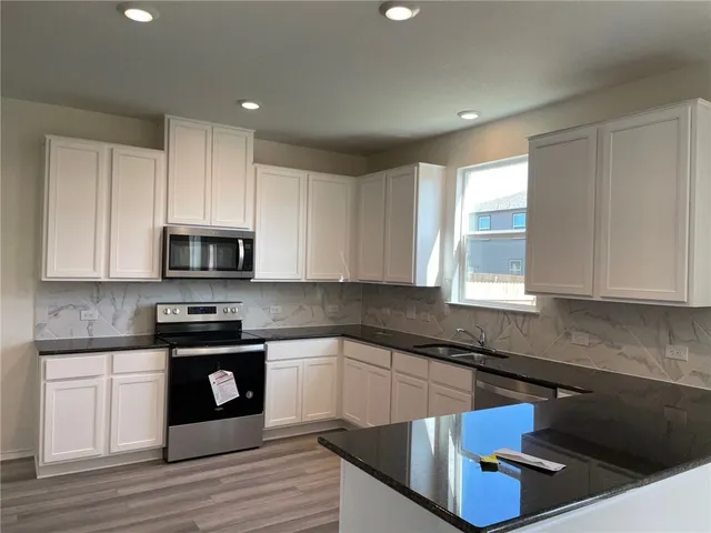 a kitchen with stainless steel appliances granite countertop a sink dishwasher a stove and a microwave oven with white cabinets