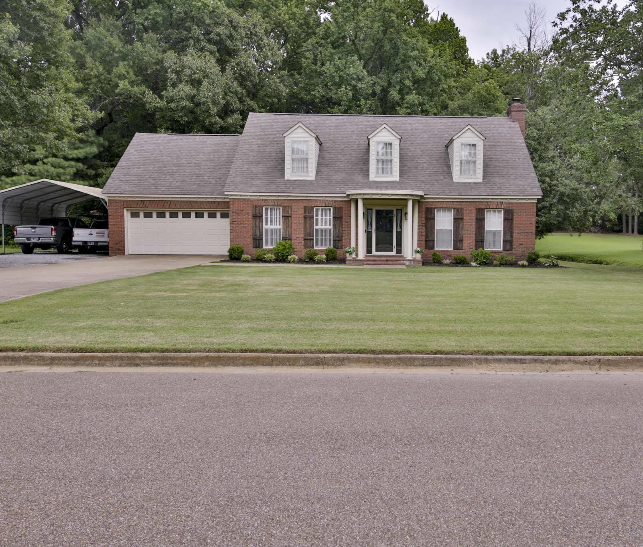 Traditional brick exterior with white trim, three dormer windows, a covered front entry, an attached two-car garage, and an additional carport