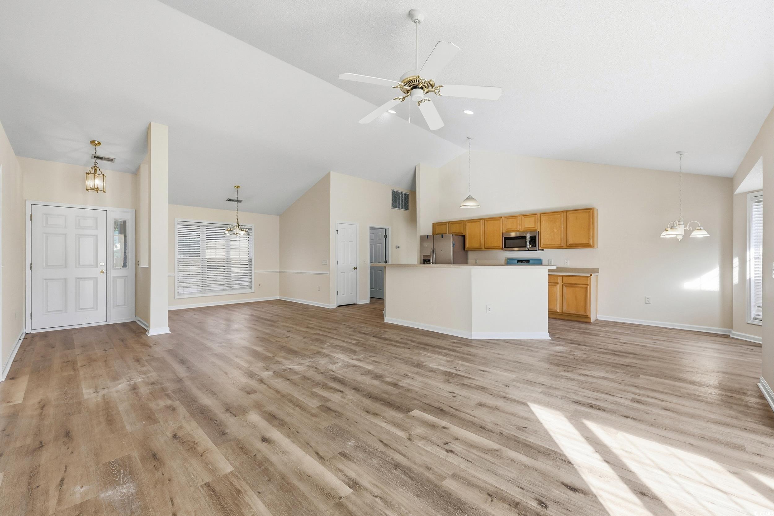 Unfurnished living room featuring a chandelier, light wood-type flooring, high vaulted ceiling, and a ceiling fan