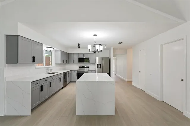 a large white kitchen with granite countertop a stove a sink a refrigerator and white cabinets