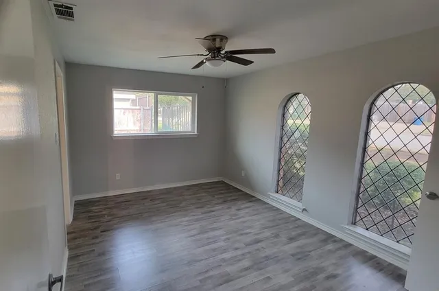 an empty room with wooden floor fan and windows