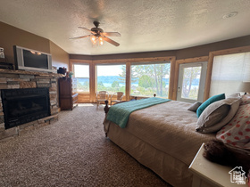 1940 East Shore Road St. Charles, ID 83272 - Photo 30 of 64 Bedroom with carpet, multiple windows, a stone fireplace, a ceiling fan, and a textured ceiling