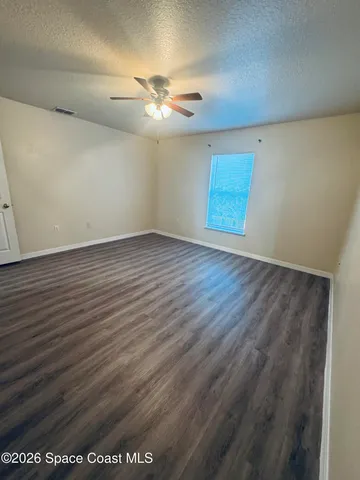 an empty room with wooden floor fan and windows