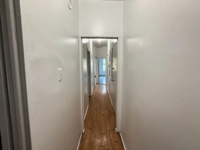 a view of a hallway with wooden floor and a bathroom