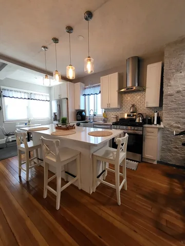 a kitchen with stainless steel appliances granite countertop a stove top oven a sink a dining table and chairs with wooden floor