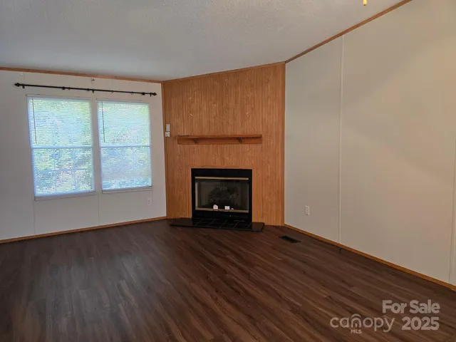 a view of an empty room with wooden floor fireplace and a window