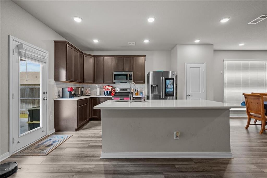 3501 Beutel Road Lorena, TX 76655 - Photo 7 of 33 Kitchen with dark brown cabinets, appliances with stainless steel finishes, backsplash, light countertops, and an island with sink