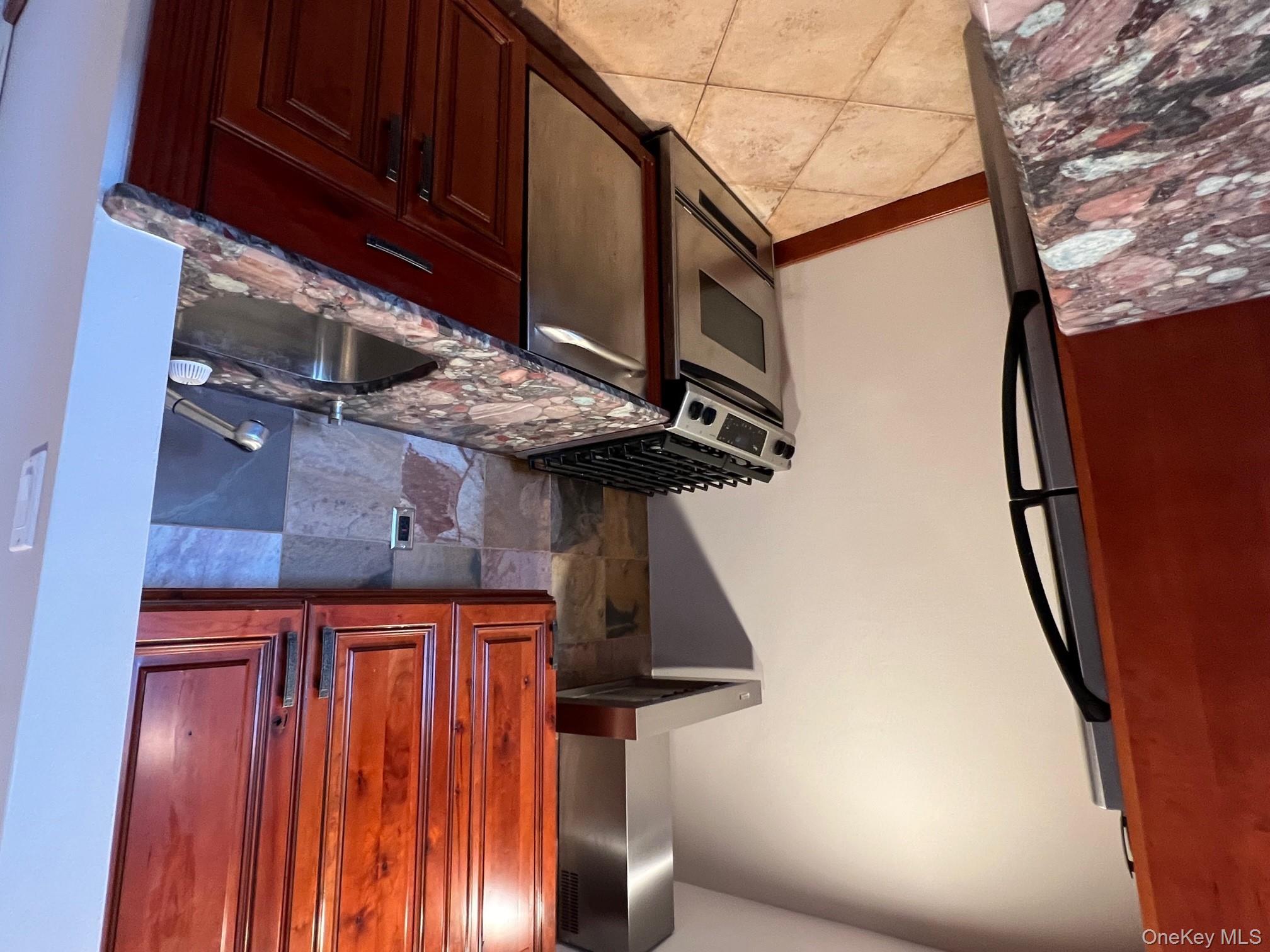 310 Riverside Boulevard, Unit 5H Long Beach, NY 11561 - Photo 6 of 13 a kitchen with granite countertop wood cabinets and a stove top oven