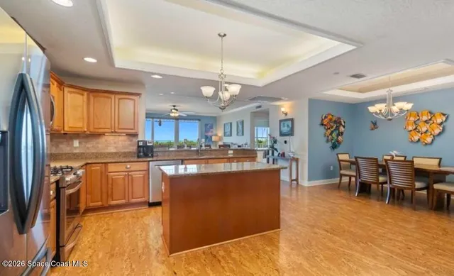 a kitchen with stainless steel appliances granite countertop a refrigerator a stove top oven a sink dishwasher a dining table and chairs with wooden floor