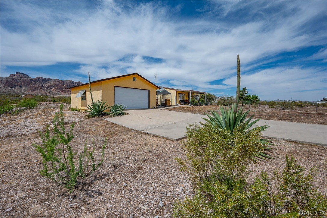 2465 Egar Road Golden Valley, AZ 86413 - Photo 78 of 98 Property with a yellow exterior and a white garage door, featuring a concrete driveway and desert landscaping