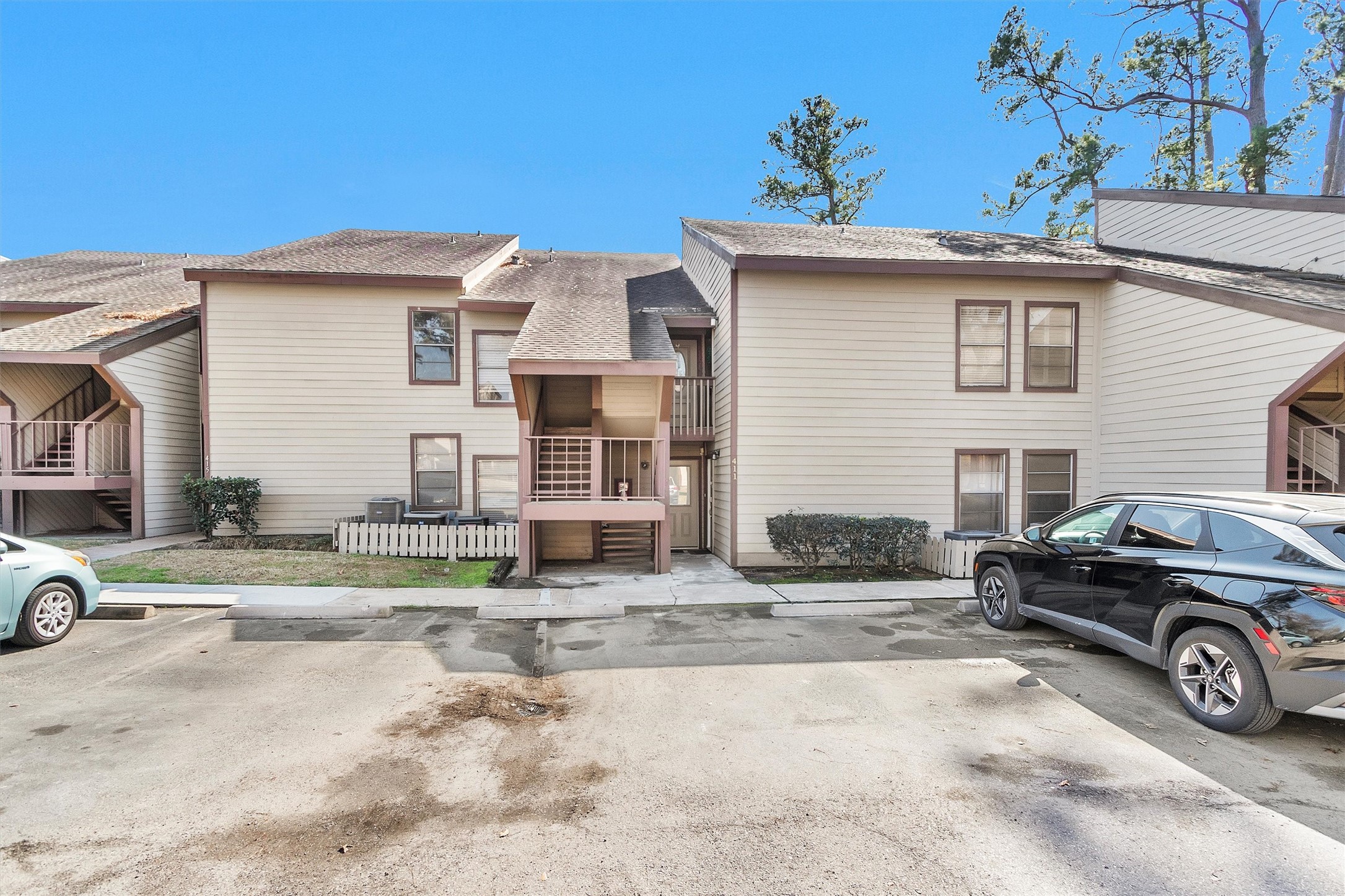 12900 Walden Road, Unit D 411 Montgomery, TX 77356 - Photo 18 of 18 Discover suburban charm in this inviting two-story townhouse featuring a beige exterior with brown trim, a cozy balcony, and shared parking, all nestled amidst lush greenery and trees.