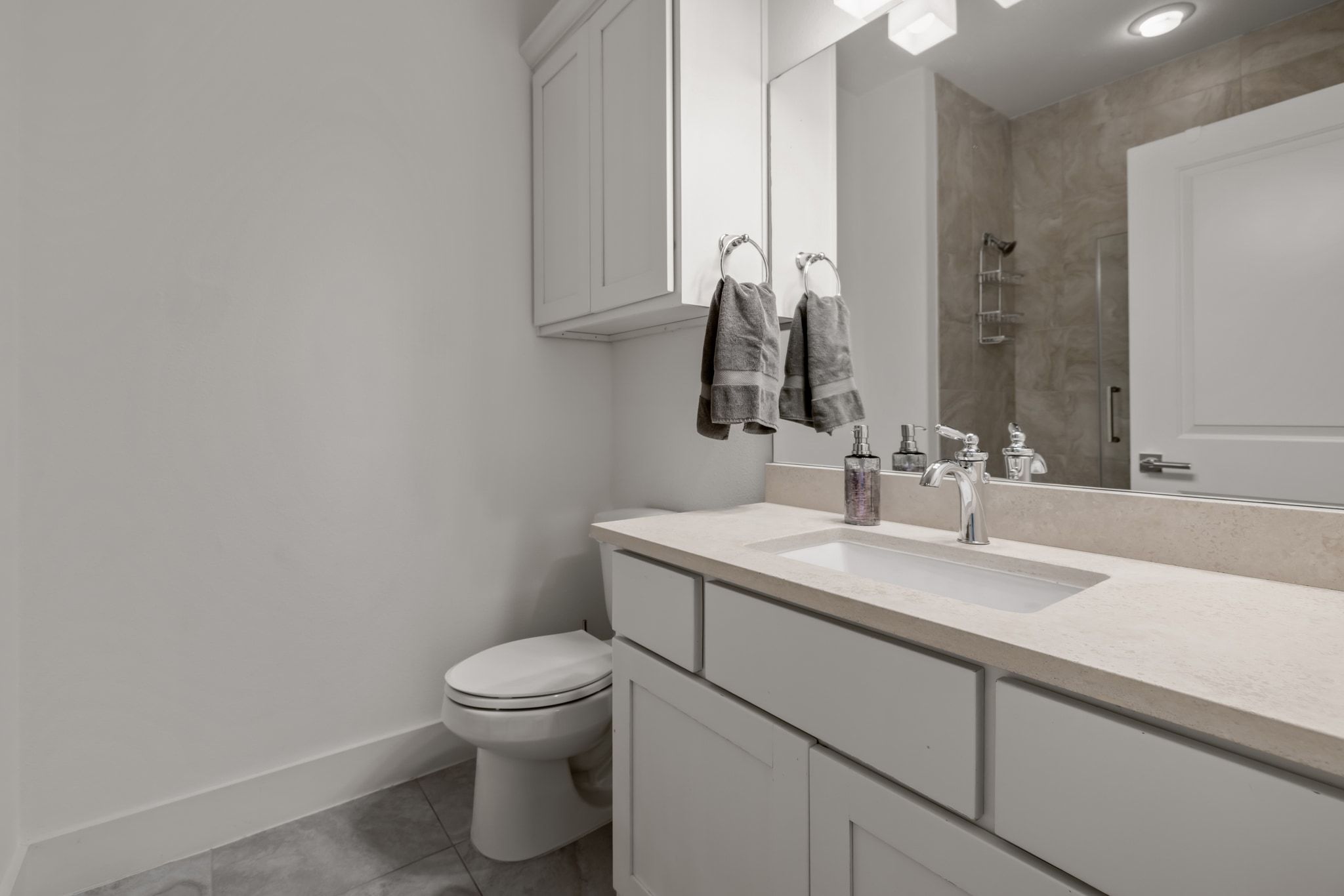 4720 Rockcliff Road, Unit 1 Austin, TX 78746 - Photo 34 of 39 A well-lit bathroom features a vanity with ample counter space and an integrated sink, complementing the tiled shower visible in the mirror's reflection.