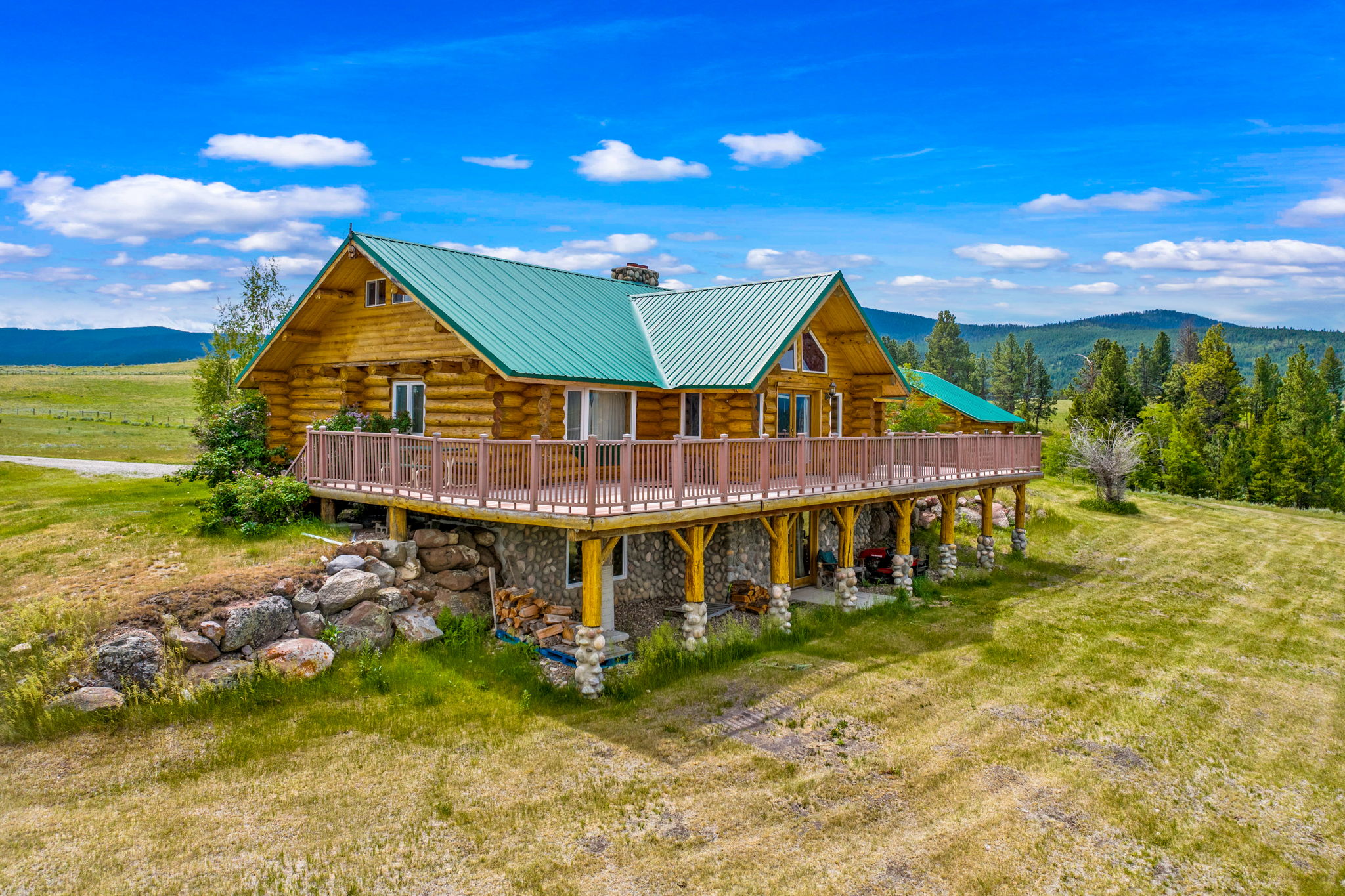 3358 Strandskov Road Lincoln, MT 59639 - Photo 55 of 80 Back of house featuring log siding, a chimney, a deck with mountain view, a metal roof, and stone siding