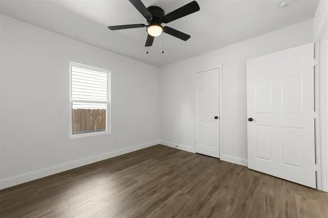 an empty room with wooden floor ceiling fan and windows