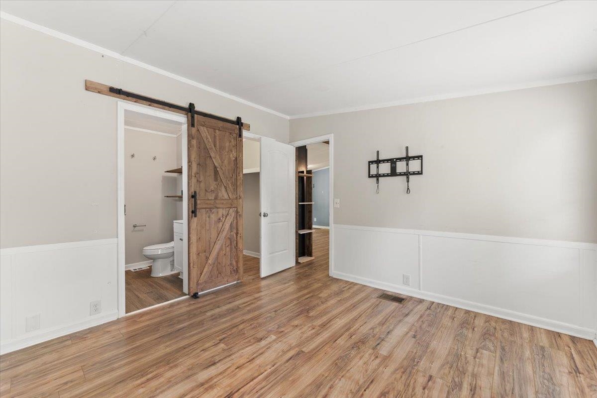 6860 Catlett Road St. Augustine, FL 32095 - Photo 13 of 36 Unfurnished bedroom featuring a barn door, light wood-type flooring, ensuite bath, and crown molding