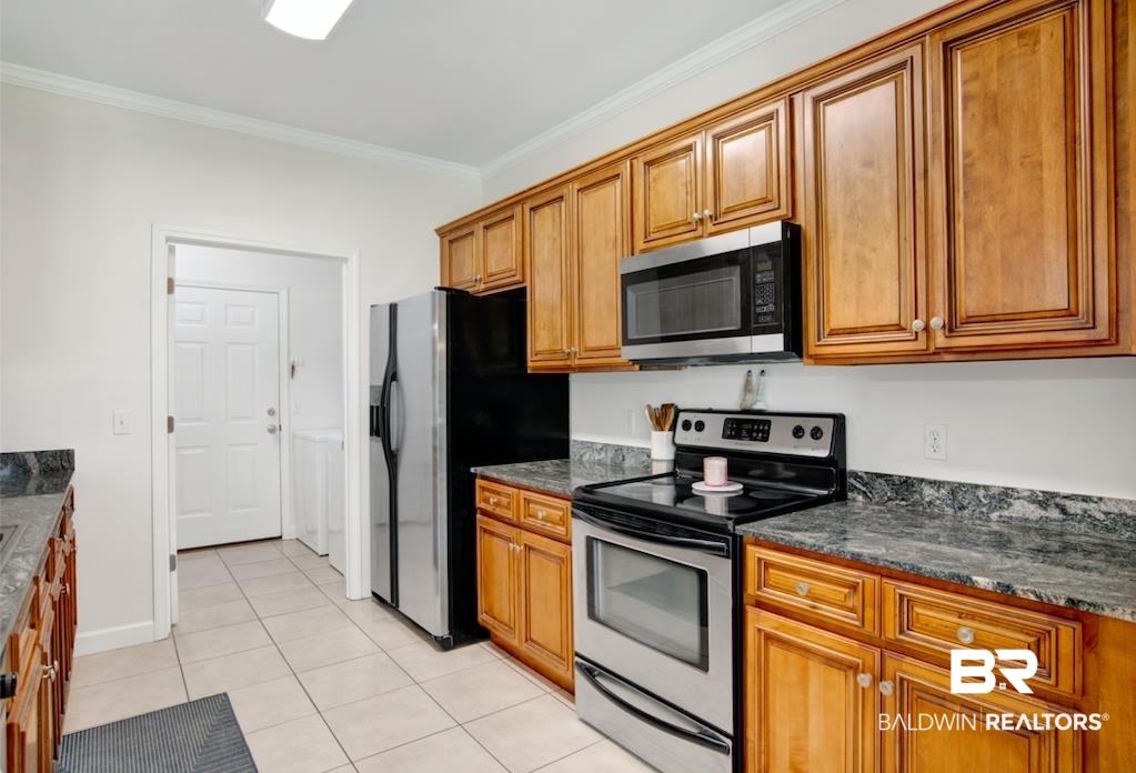 27545 Boaz Road West Loxley, AL 36551 - Photo 10 of 26 Kitchen with stainless steel appliances, brown cabinetry, ornamental molding, light tile patterned flooring, and dark stone countertops