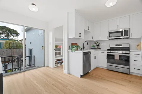 a kitchen with stainless steel appliances a stove top oven a refrigerator white cabinets and wooden floor