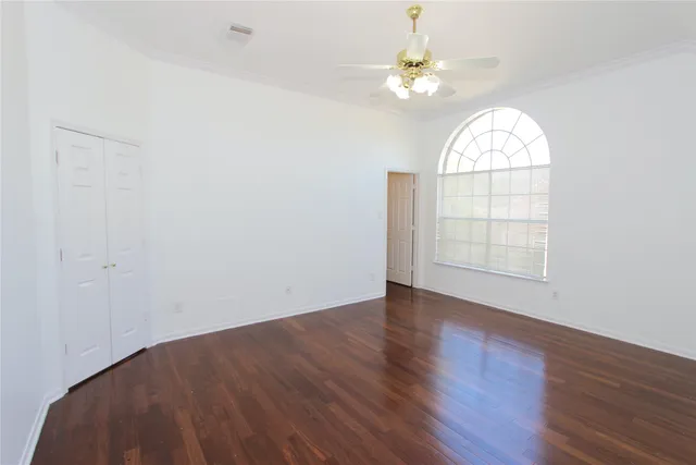 an empty room with wooden floor chandelier fan and windows