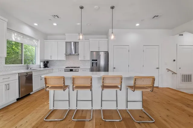 a kitchen with stainless steel appliances granite countertop a stove a sink a refrigerator and white cabinets with wooden floor