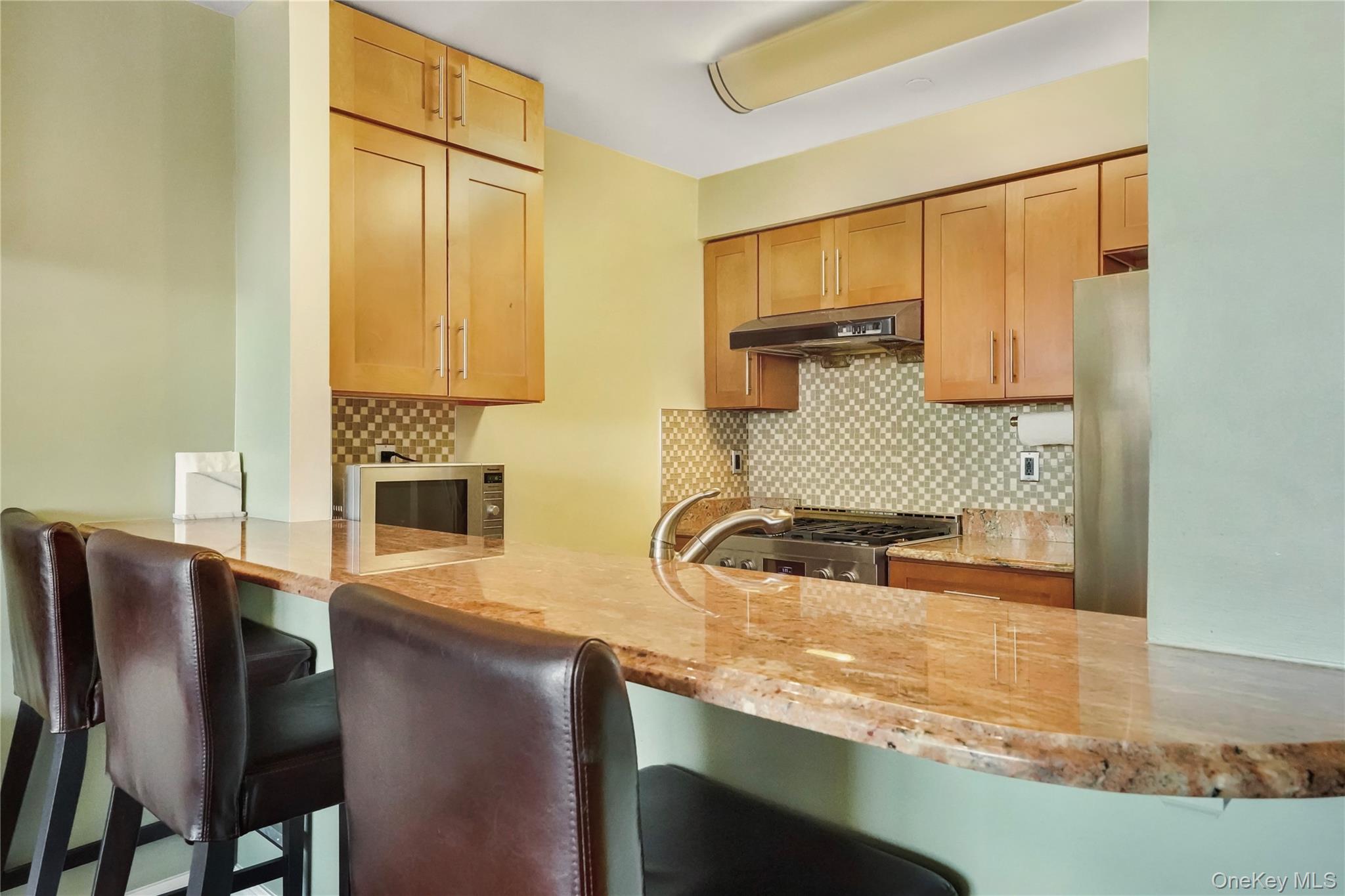 40-40 75th Street, Unit 7C Queens, NY 11373 - Photo 7 of 33 Kitchen with a kitchen bar, decorative backsplash, a peninsula, and light stone countertops