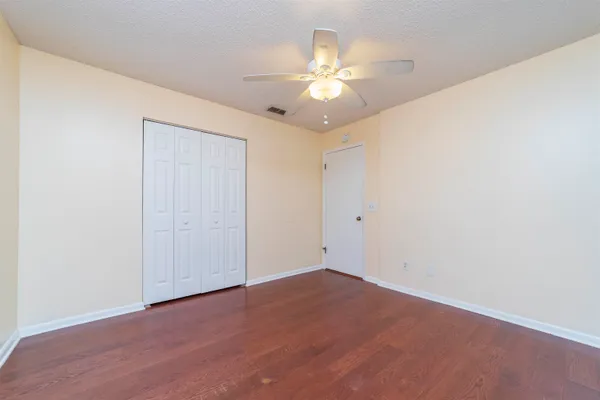 an empty room with a chandelier fan and wooden floor