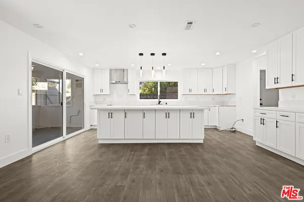 a large white kitchen with granite countertop a stove a sink and white cabinets with wooden floor