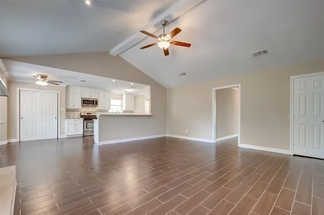 a view of an empty room with wooden floor and a kitchen