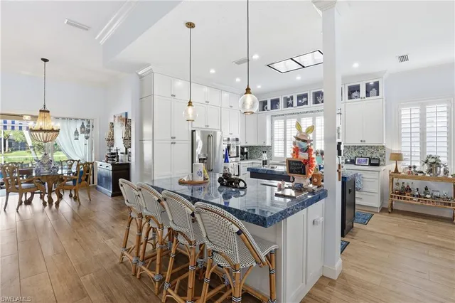 a kitchen with stainless steel appliances granite countertop a stove a refrigerator a kitchen island a dining table and chairs with wooden floor