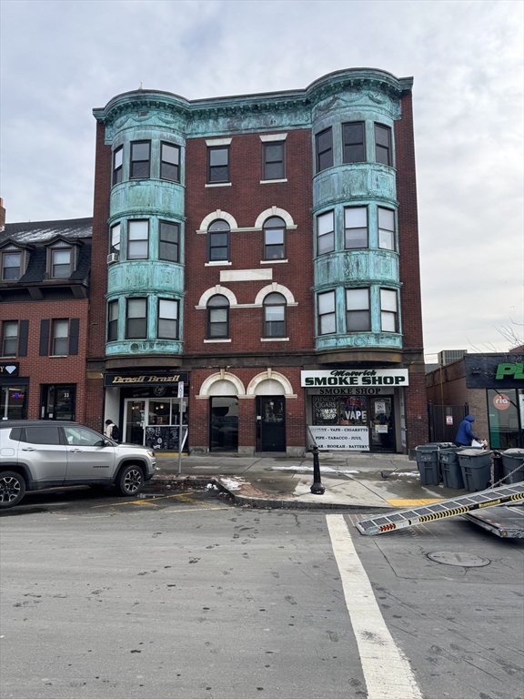 a front view of a building with lot of cars and trees