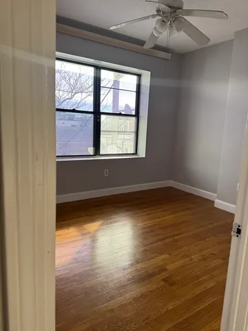 an empty room with wooden floor fan and windows