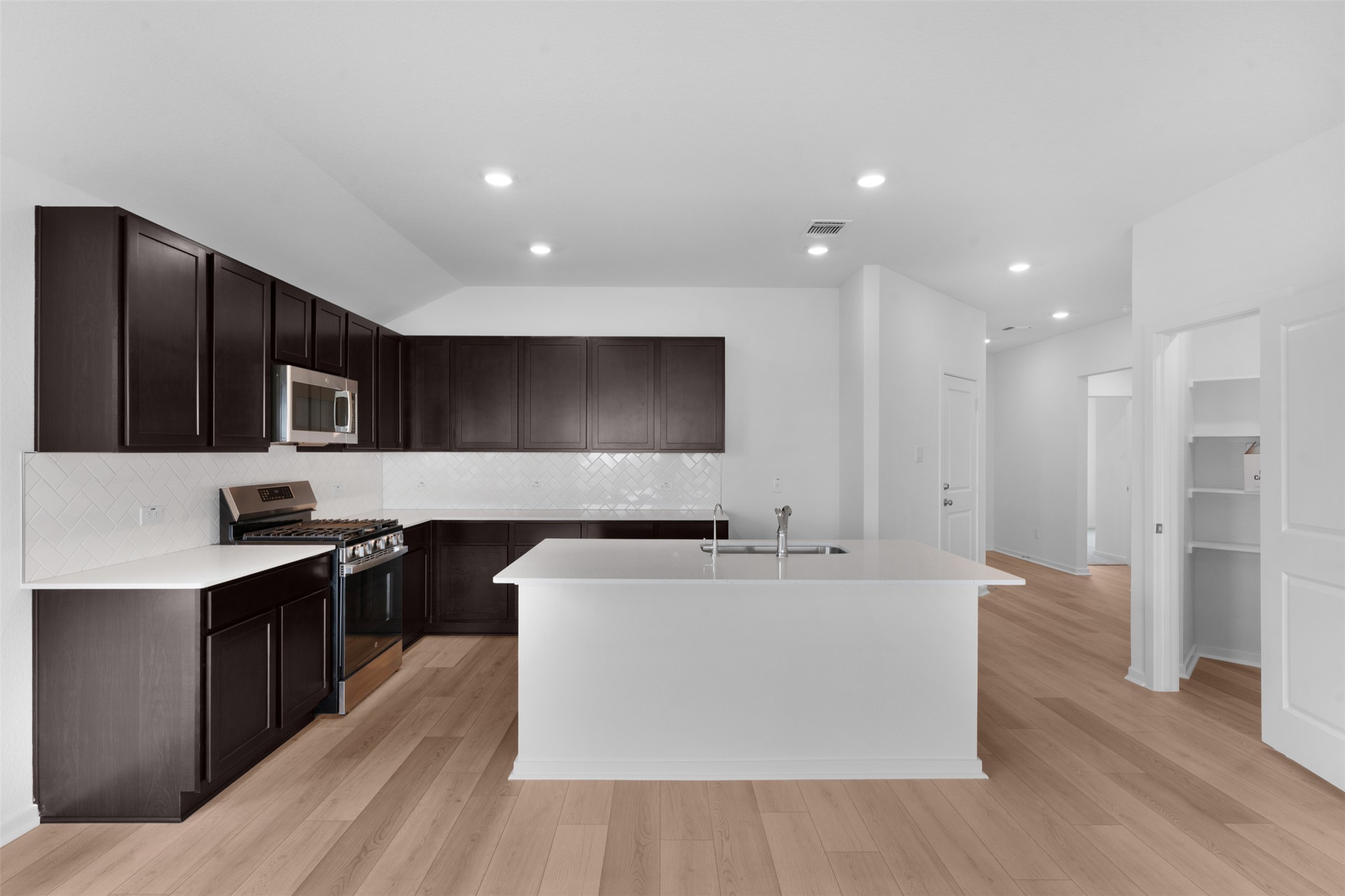 13701 Tucker Hedge Pass Elgin, TX 78621 - Photo 8 of 21 Modern kitchen featuring dark wood cabinetry, light countertops, stainless steel appliances, and a white subway tile backsplash